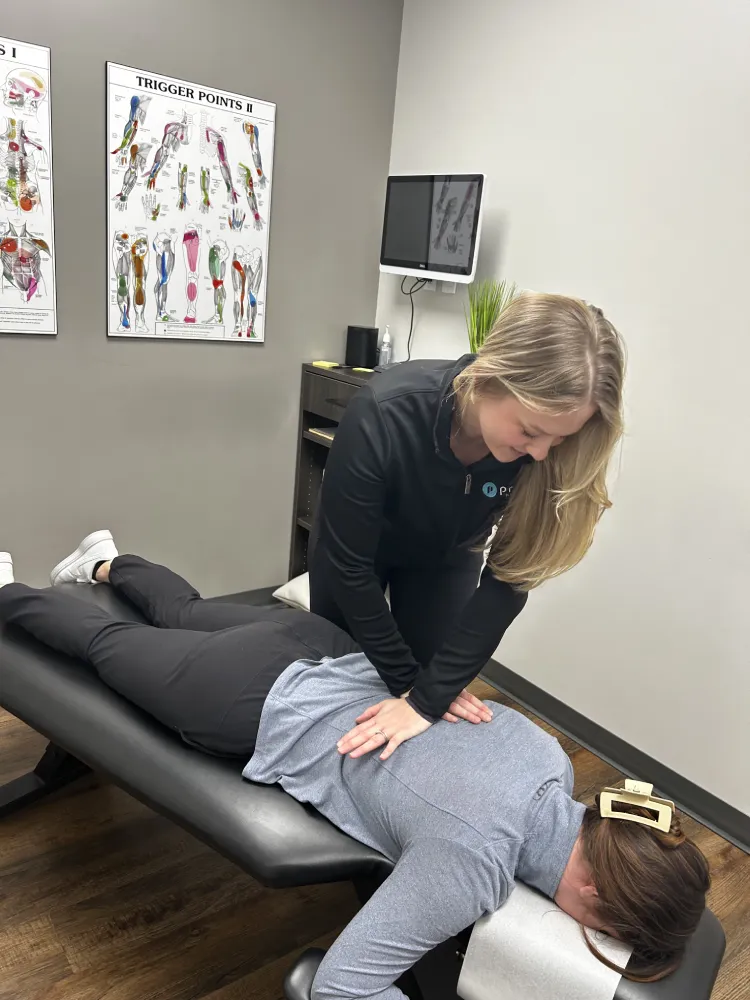Female chiropractor performs adjustment on woman's middle back as she lays on treatment table